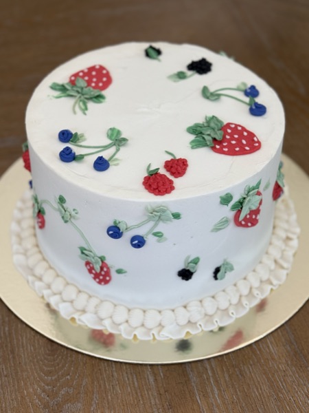 White cake painted and piped with strawberries, raspberries, blueberries, and blackberries