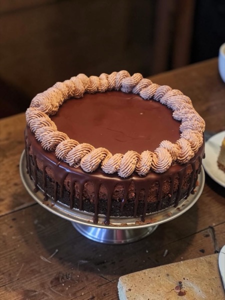Chocolate cheesecake with a smooth ganache top, piped mocha buttercream rosette border, and chocolate ganache drips down the sides