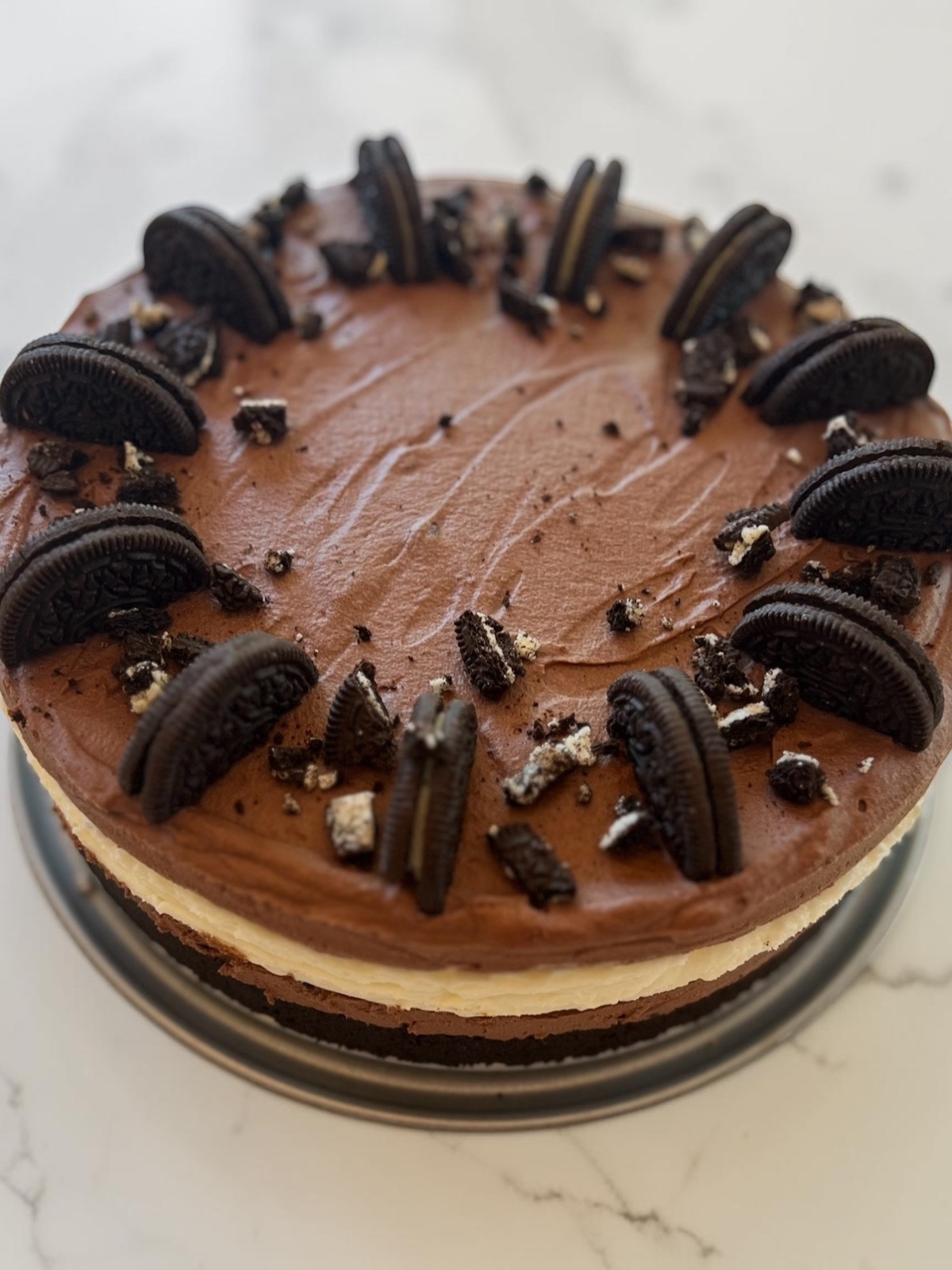 Vanilla cheesecake topped with dark chocolate frosting and ringed with halved chocolate sandwich cookies and crumbs