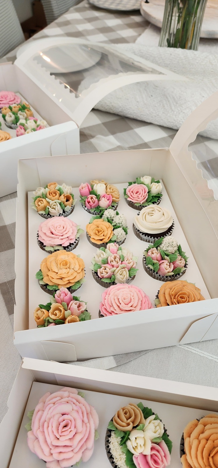 A box of buttercream flower cupcakes with roses, tulips, and hydrangeas in pink, peach, and cream