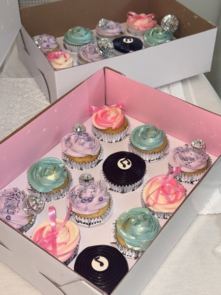 Angled view of two boxes of the vinyl and disco cupcakes side by side showing the variety of rosette swirls, disco balls, and vinyl-record toppers