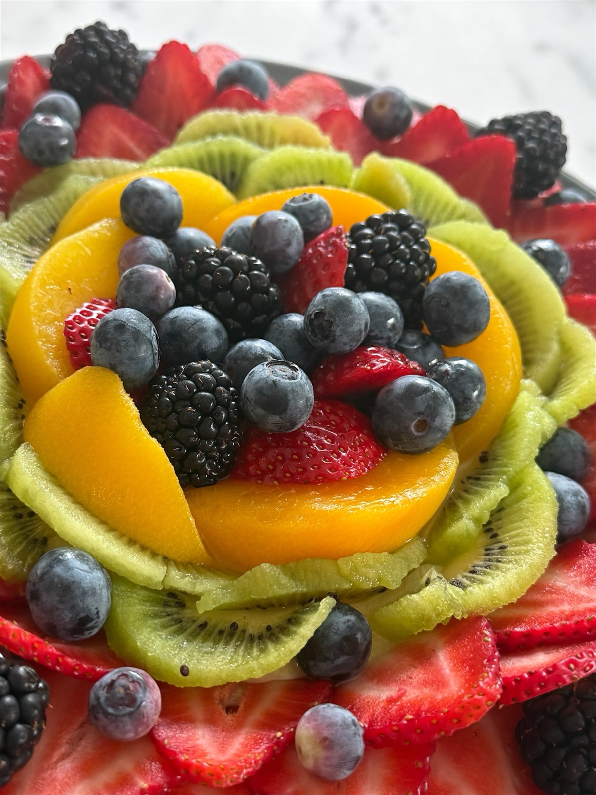 Fruit tart with mango, kiwi, blueberries, blackberries, and strawberries, side angle