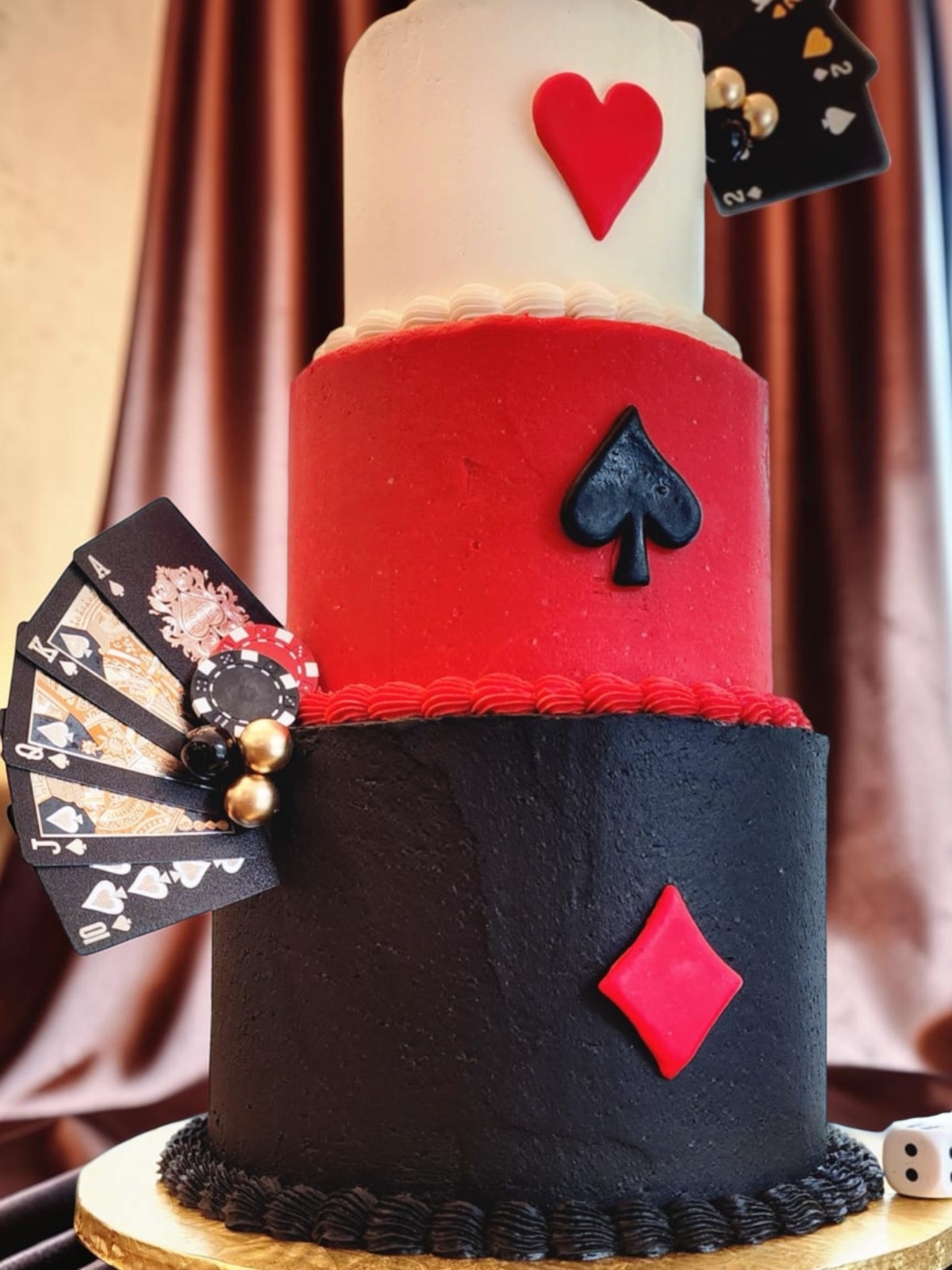Close-up angle of the playing-card cake showing the heart, spade, and diamond tiers with a fan of cards and a poker chip